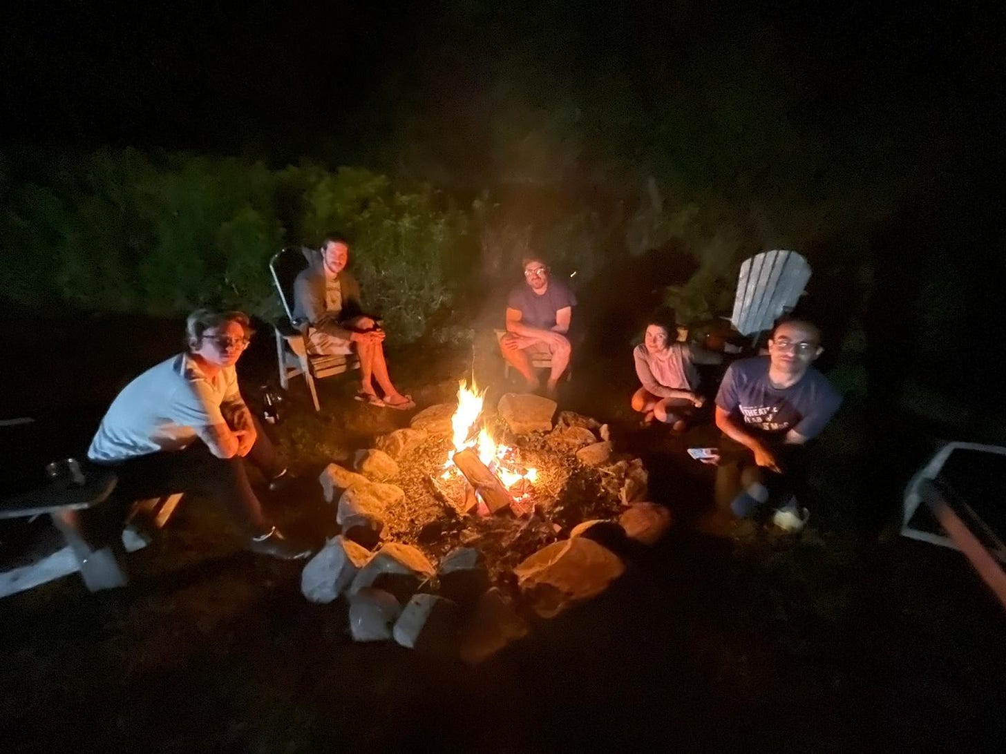 A group of young people sit around a fire at night