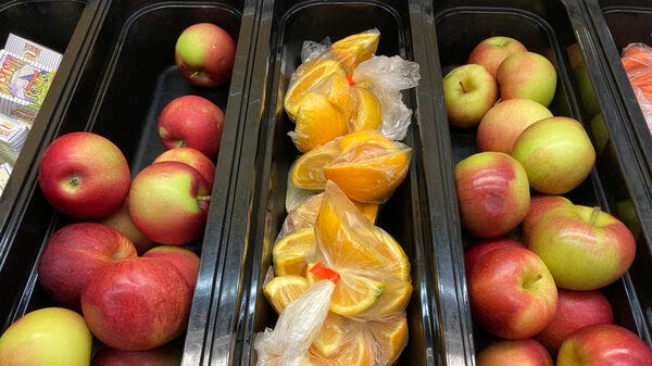 Whole apples and orange slices arranged in rows for school lunch.