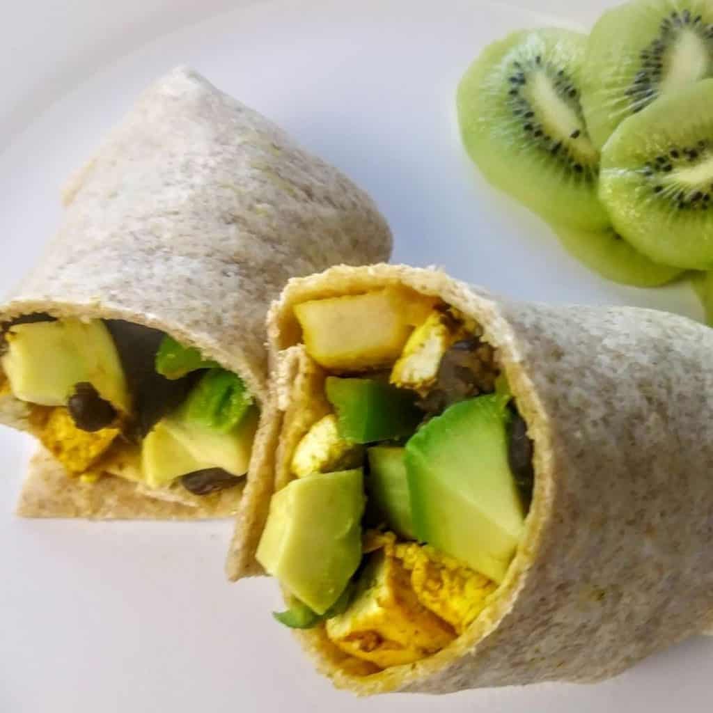 breakfast burrito with scrambled tofu and slices kiwis on the  plate