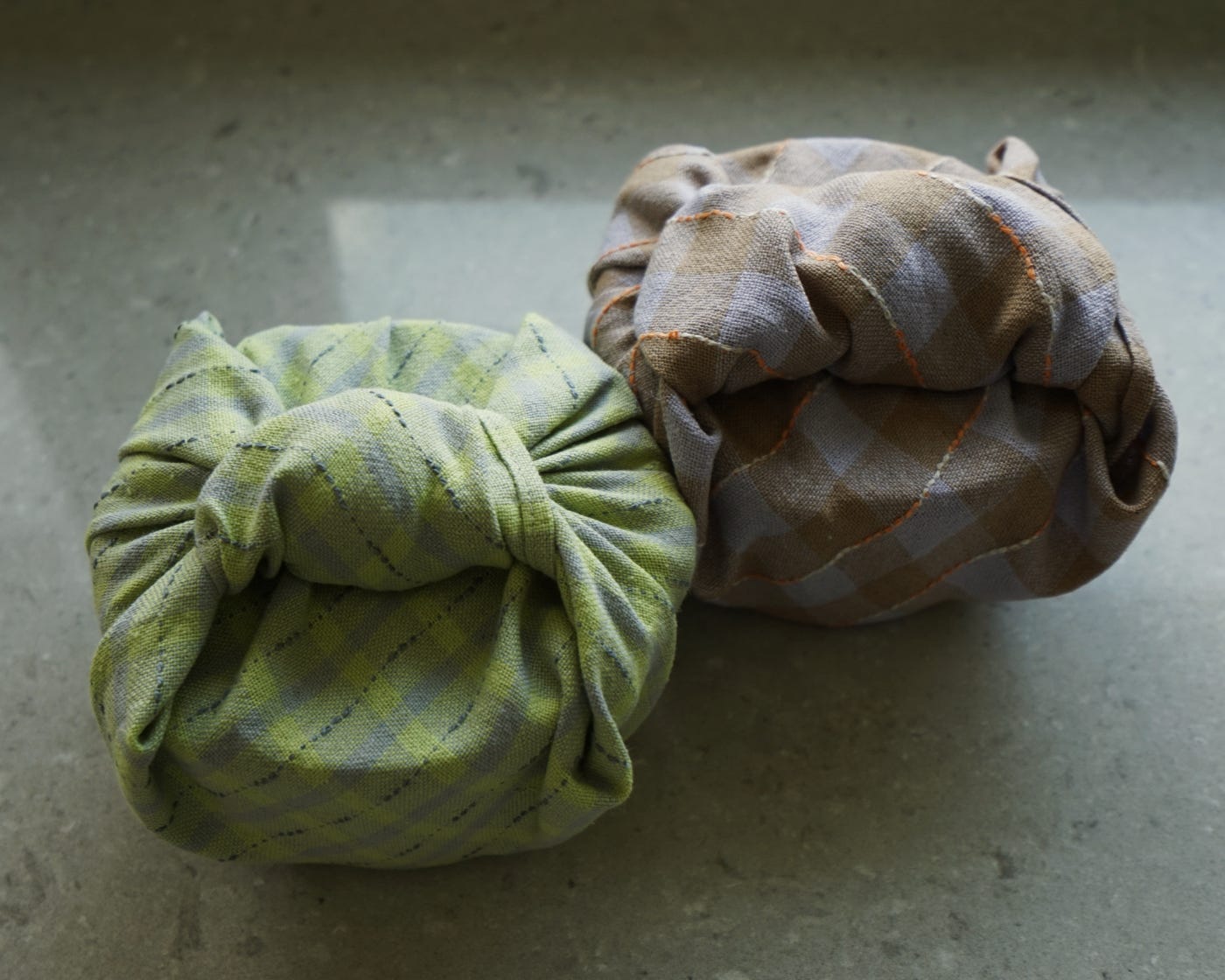 Two containers wrapped in cloth sit next to each other on a countertop. 