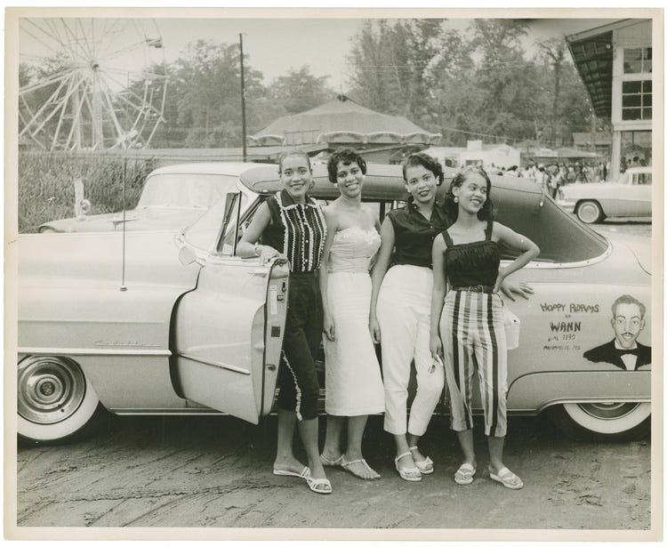 Four women pose in front of a car