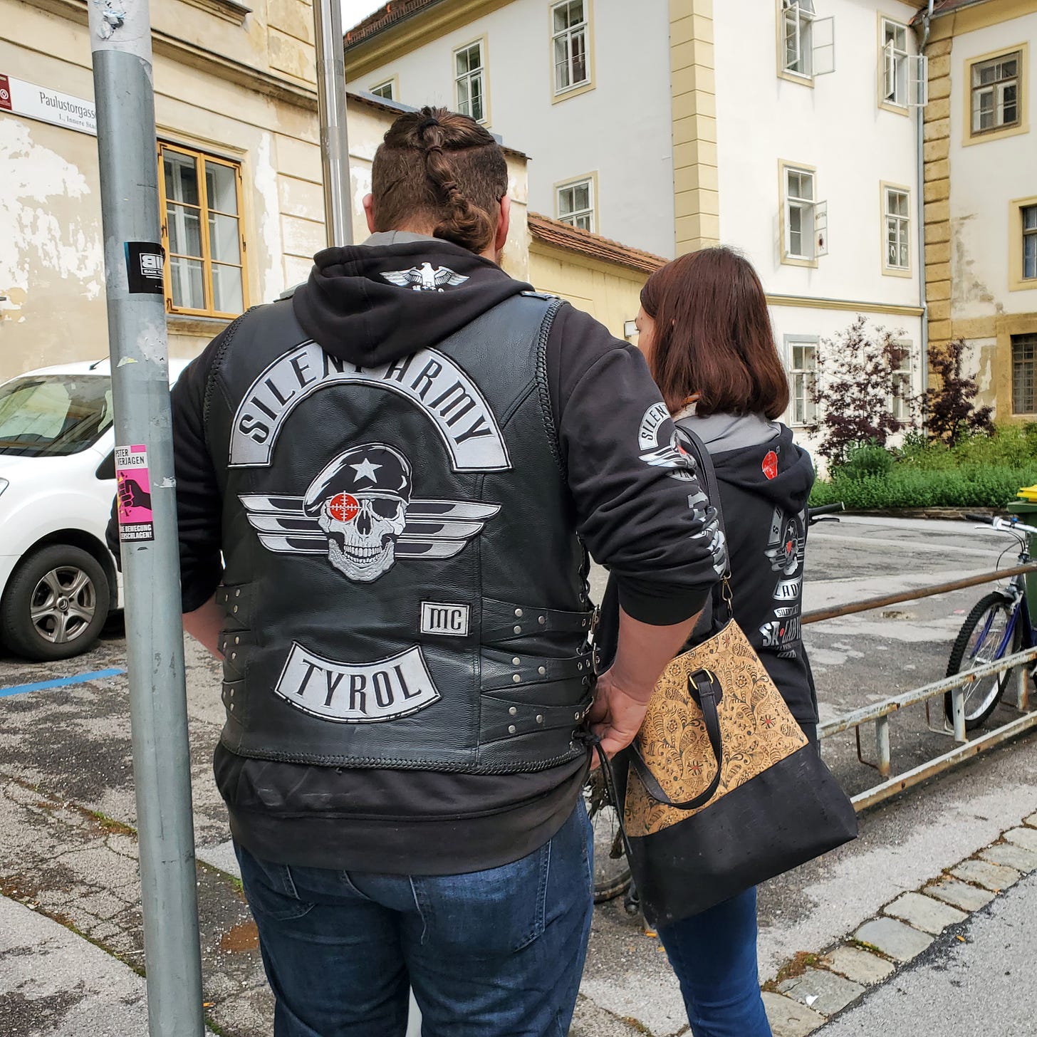 A heterosexual white couple both wearing “Silent Army Tyrol” jackets with Nazi-styled graphics and, on the man’s hoodie, an actual Nazi symbol.