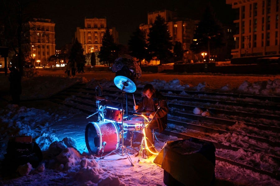 A street musician plays an illuminated drum set at night.