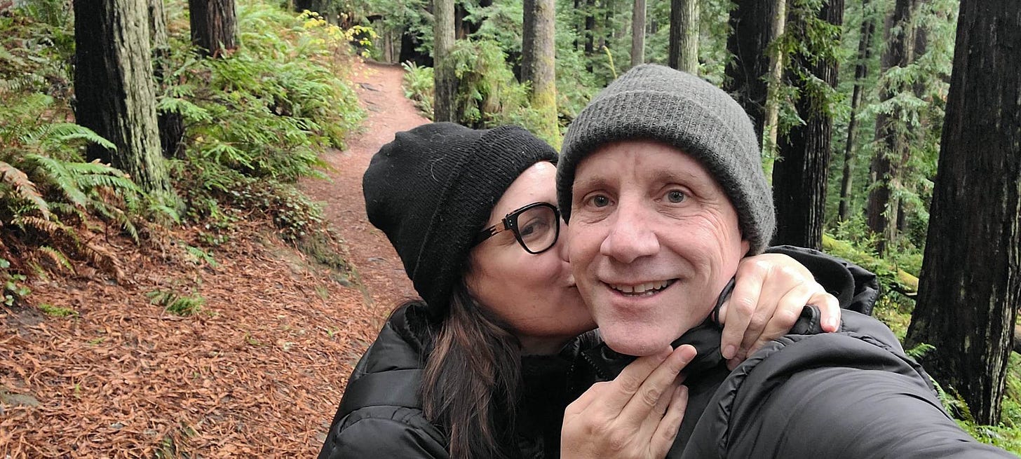 Photo of Deb and I in the forest. Deb is kissing my cheek.