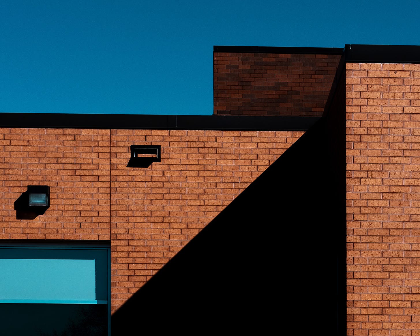 The facade of an orange brick building is covered with shadows under a clear blue sky