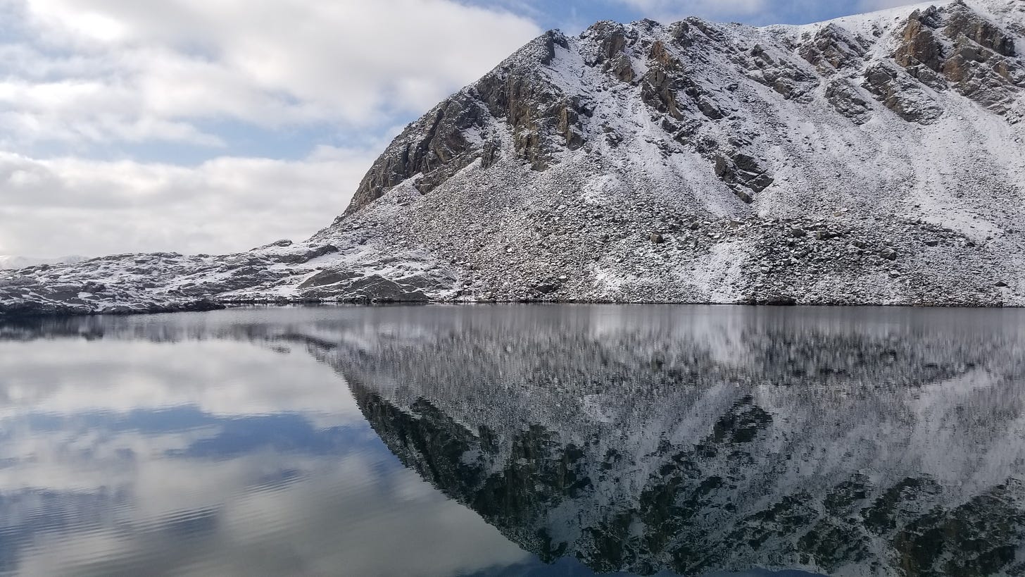 a snow-dusted mountain ridge, reflected perfectly in an alpine lake