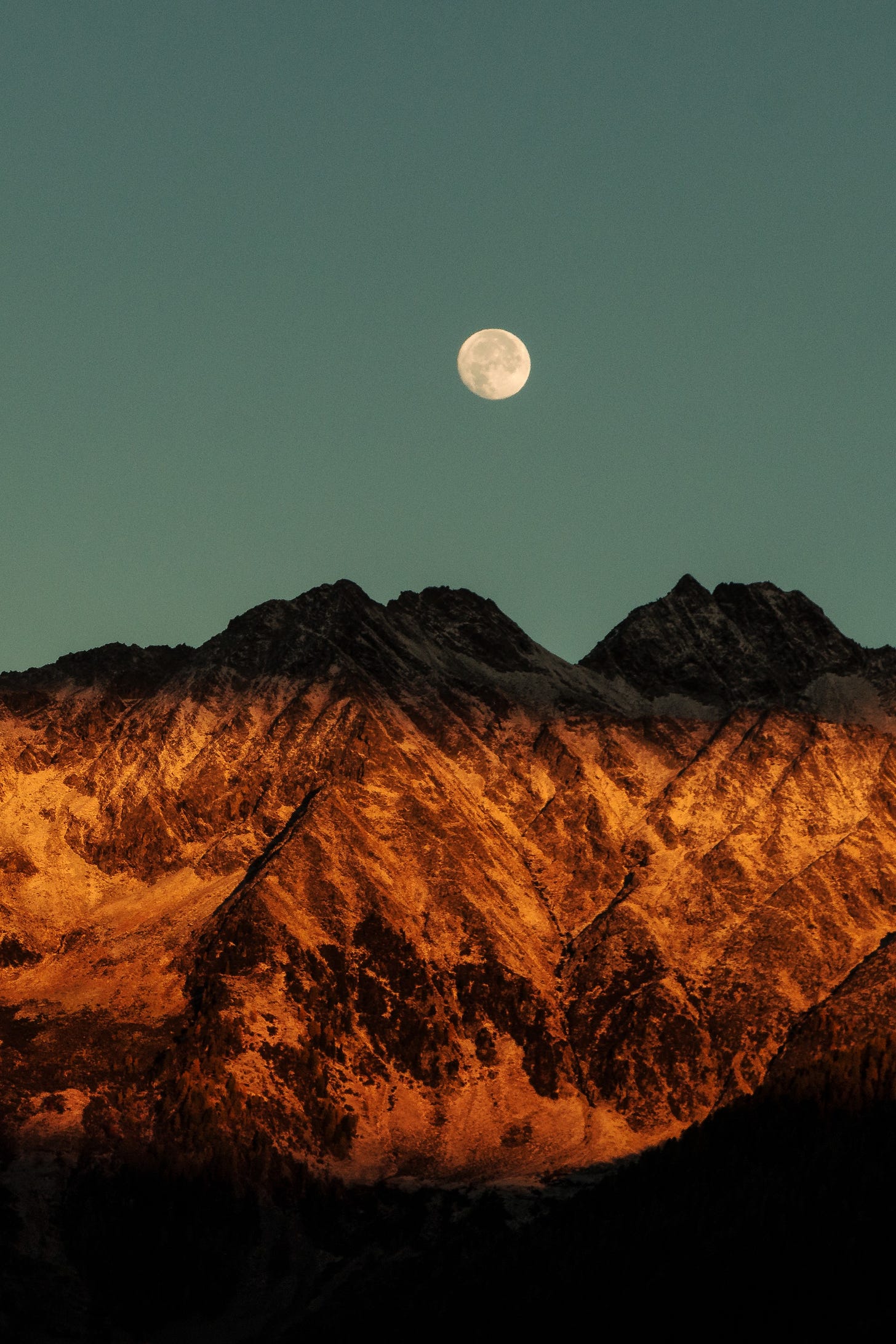 Full moon visible by day over mountains