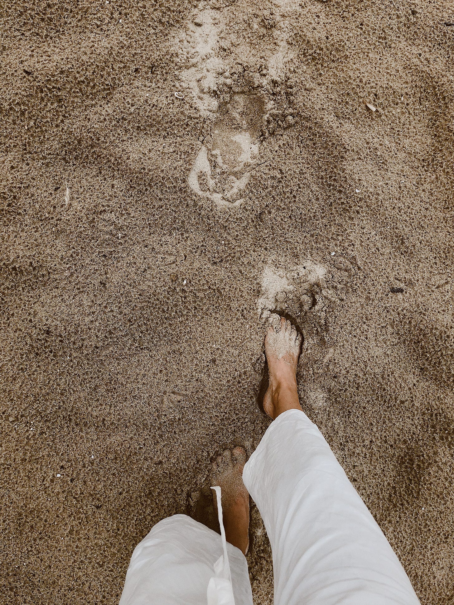 person's feet as they walk across the sand