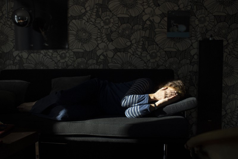 A woman lying sideways on a sofa covering her face with her hands.