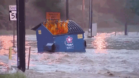 Dumpster on fire floating down a flooded roadway