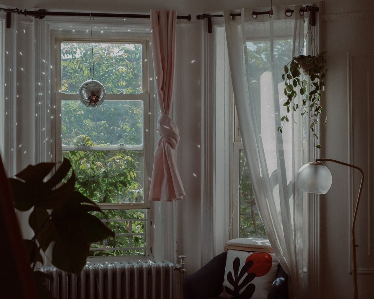 photo of two bay windows with plants hanging from the curtain and a disco ball illuminating the living room with droplets of light.