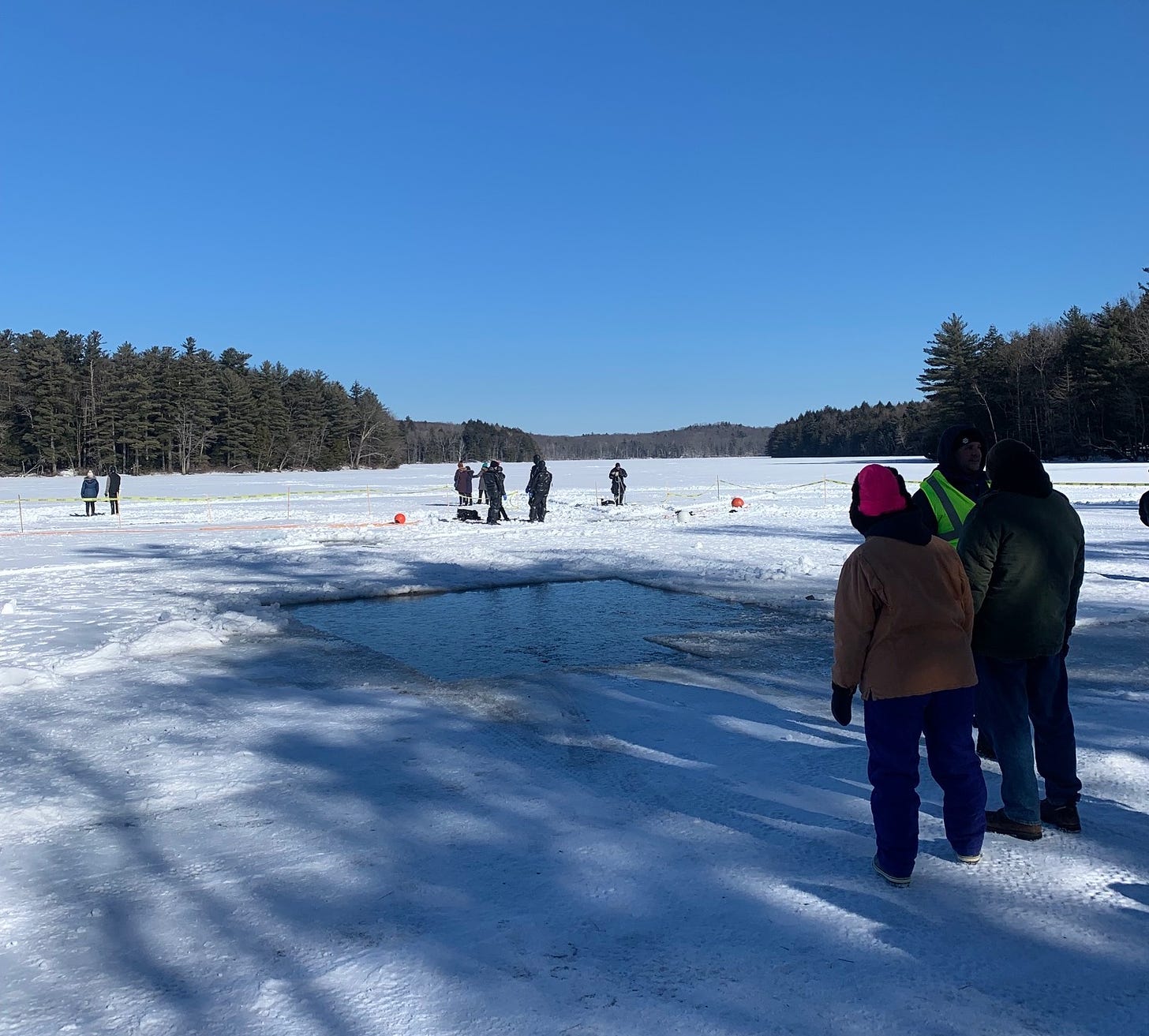 View of a frozen lake with scattered people and a square hole cut into the ice