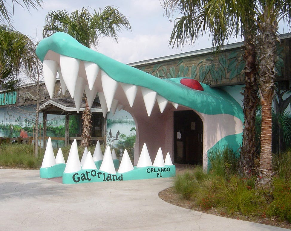A building with a very large alligator mouth leading up to the door, like the door is his throat and he's swallowing you. It is very cartoonish. On his bottom lip is written "Gatorland Orlando FL". Palm trees surround him A building with a very large alligator mouth leading up to the door, like the door is his throat and he's swallowing you. It is very cartoonish. On his bottom lip is written "Gatorland Orlando FL". Palm trees surround him