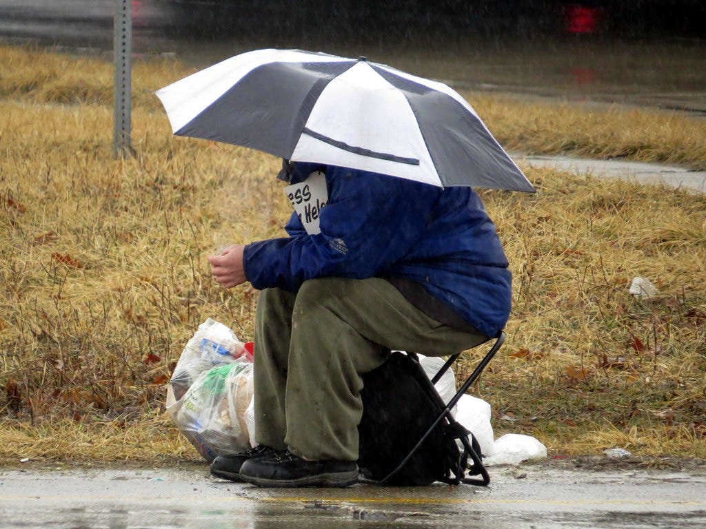 A panhandler brings his umbrella and seat.