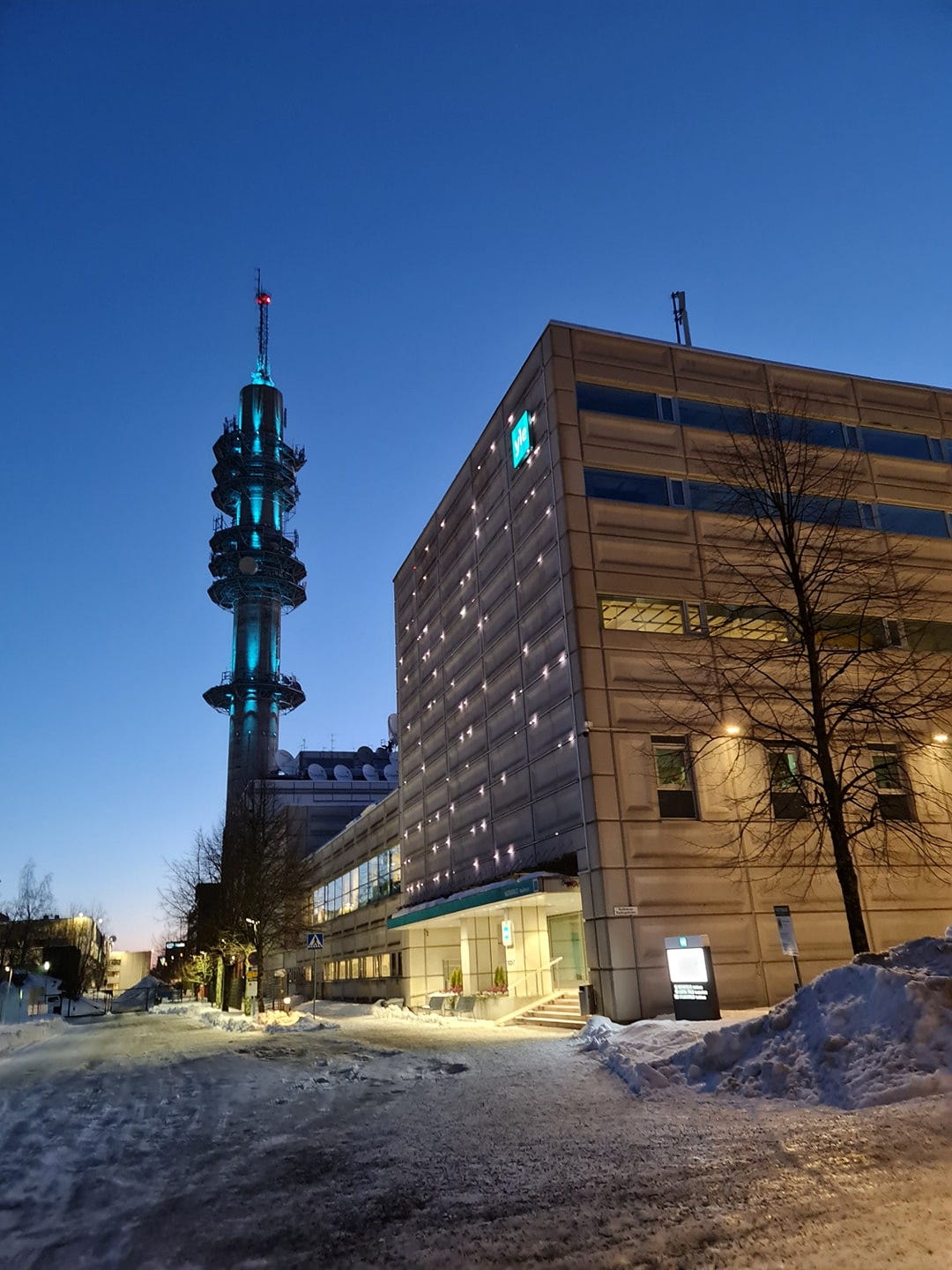 En vintrig bild av radiotornet i Böle i Helsingfors intill ett hus i grå betong