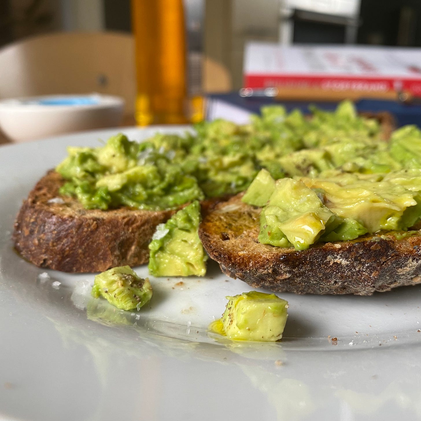 plate topped with two slices of seeded sourdough bread and smashed avocado