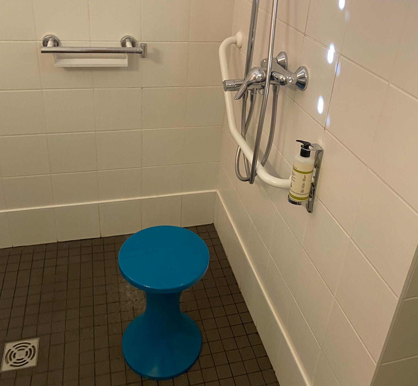 photo of accessible shower in hotel room. a blue plastic stool in a front of a shower head