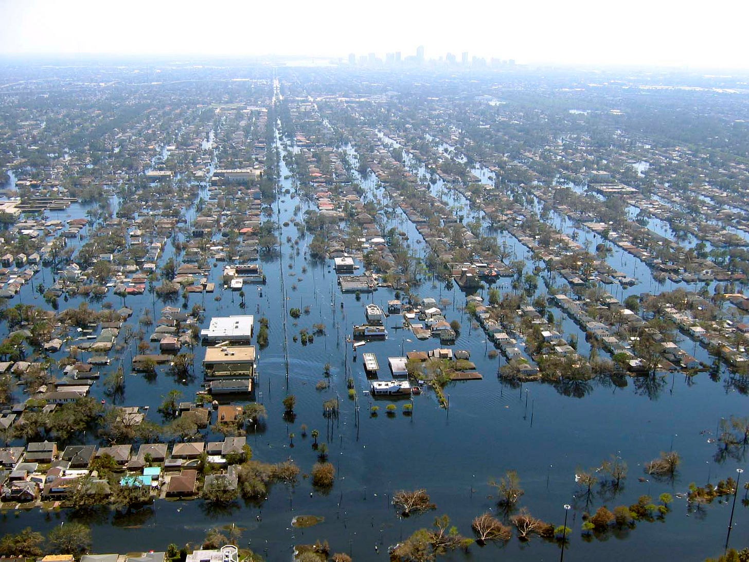 The flooding of New Orleans following Hurricane Katrina. There are rows of houses, with a lot of water everywhere. Downtown can be seen in the mist in the distance