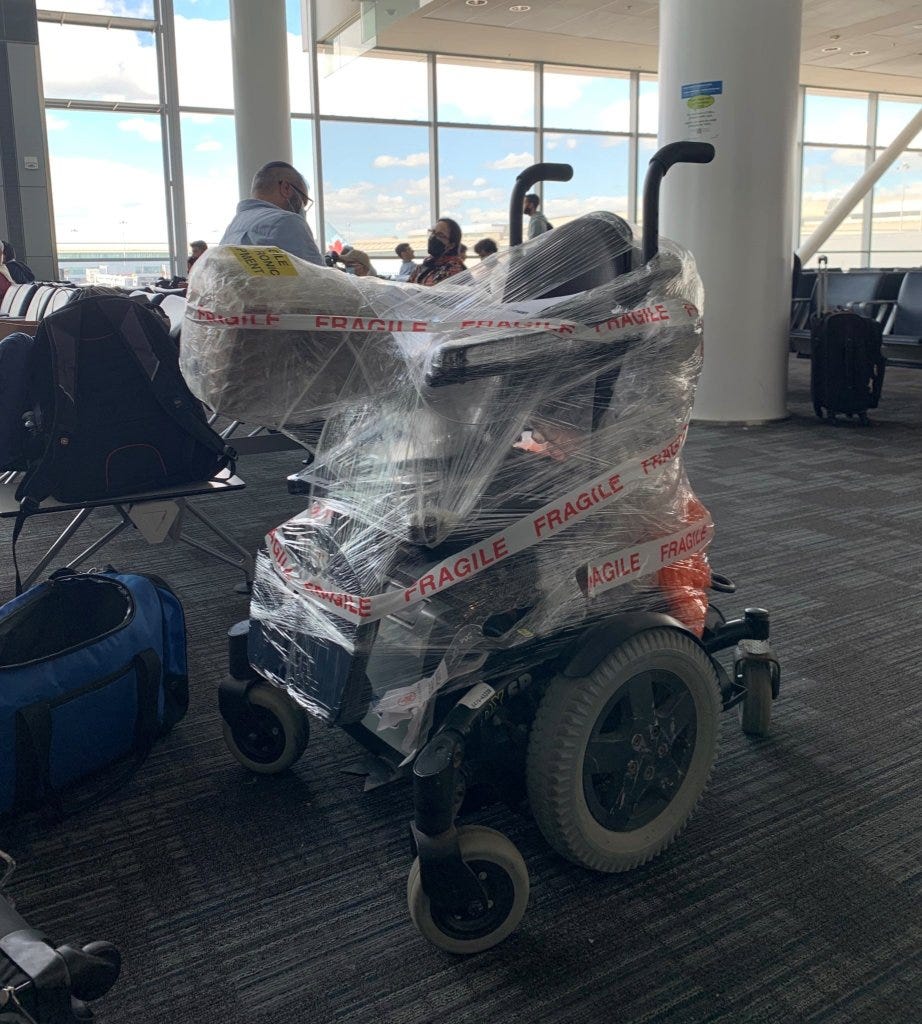 A powerchair sits in the gate area of an airport, wrapped in plastic and tape that says FRAGILE FRAGILE FRAGILE.
