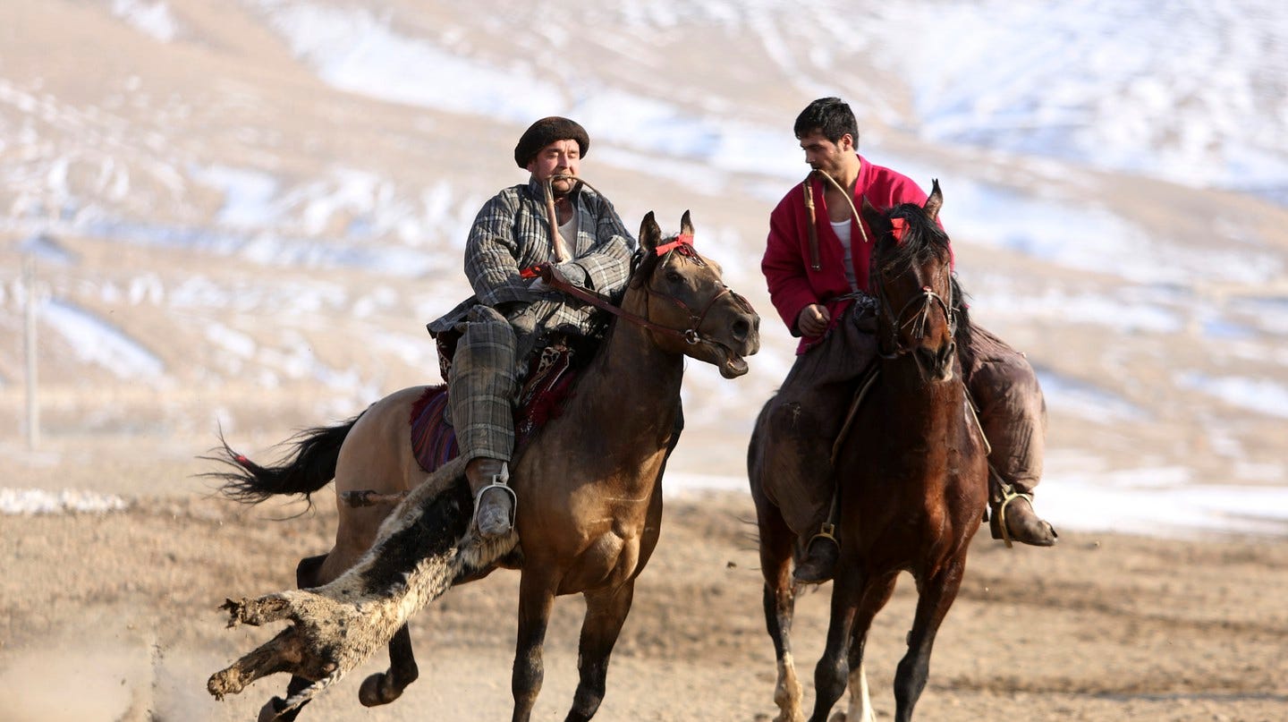Two buzkashi players, one dragging a "buz" (goat) alongside his horse
