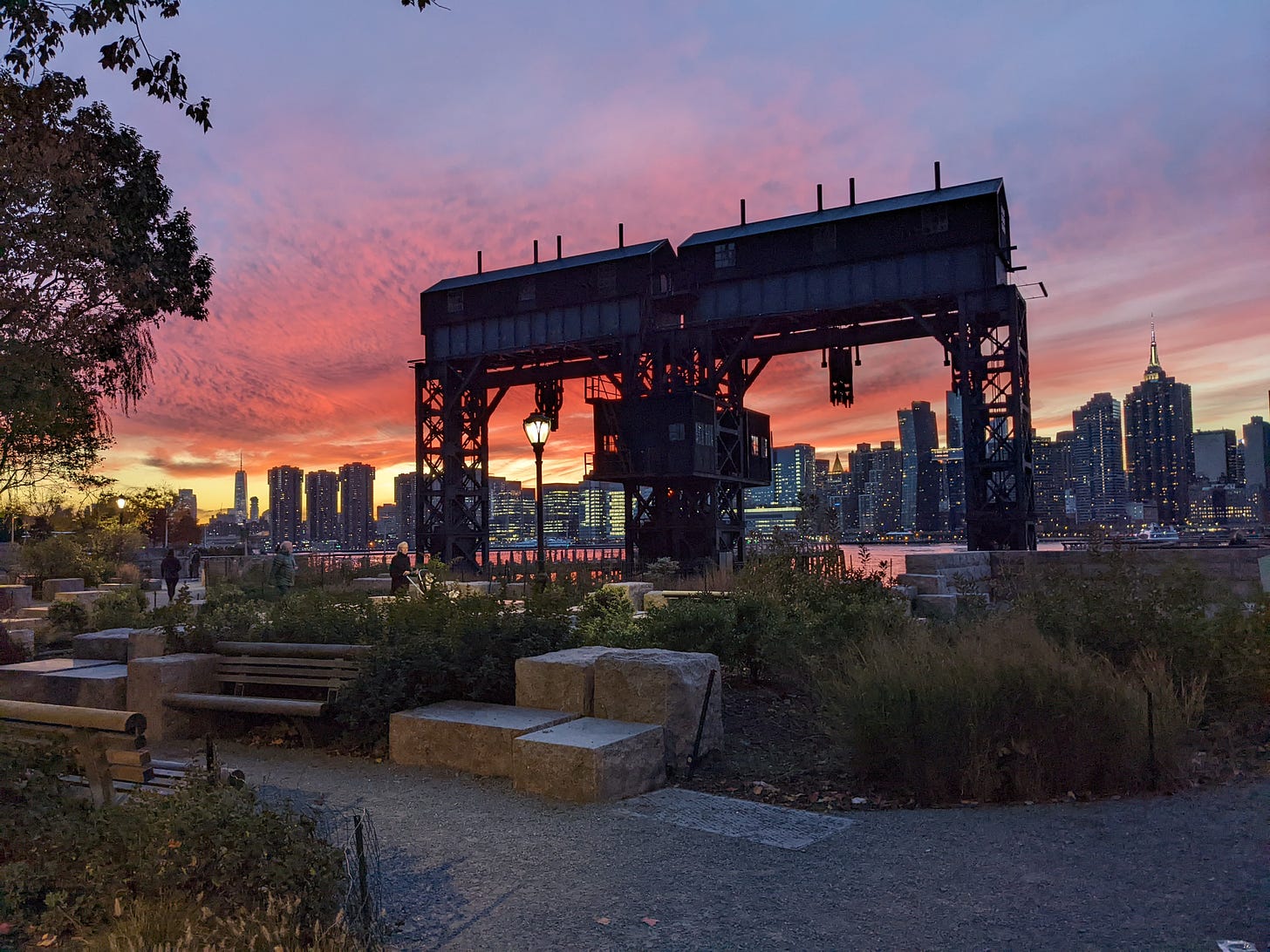 Sun set in Hunters Point Park. An industrial crane stands in the foreground, in the background the river and New York City skyline.