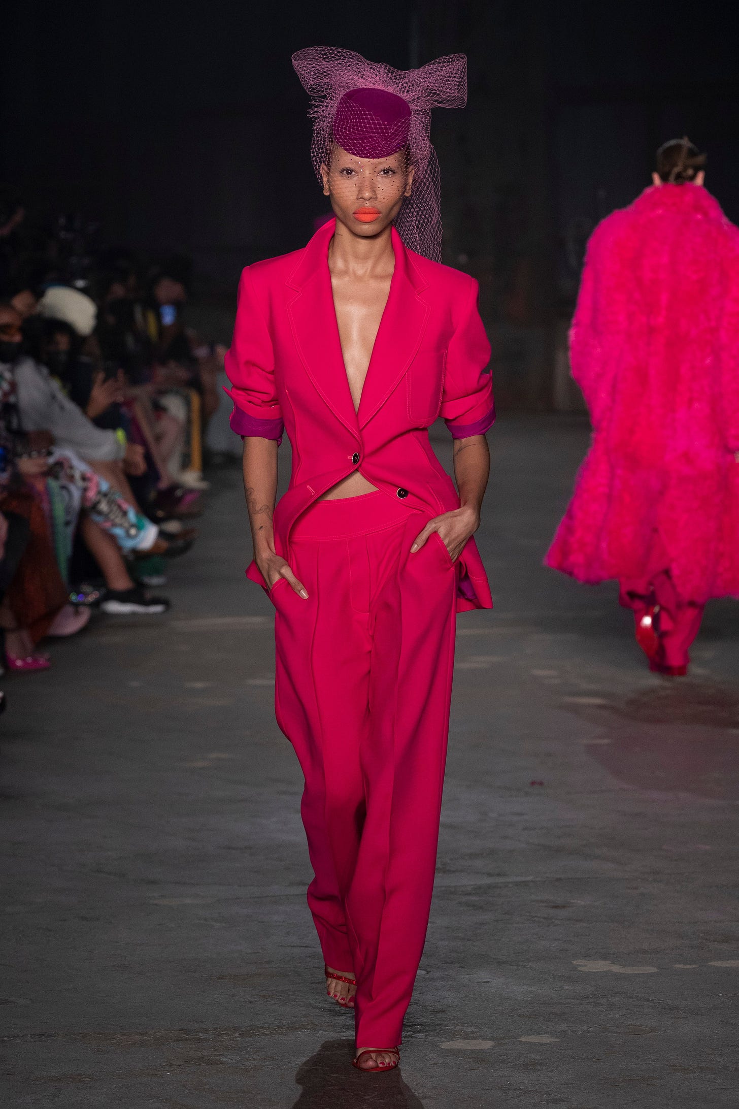 an image from Christopher John Rogers' Resort 2023 collection, featuring a model in a fuschia/hot pink suit and a netted pillbox hat.