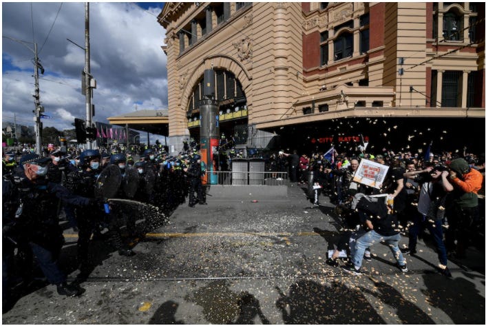A mob of riot police wearing black uniforms and carrying shields pepper spray a group of protestors outside Melbourne's Flinders Street Station