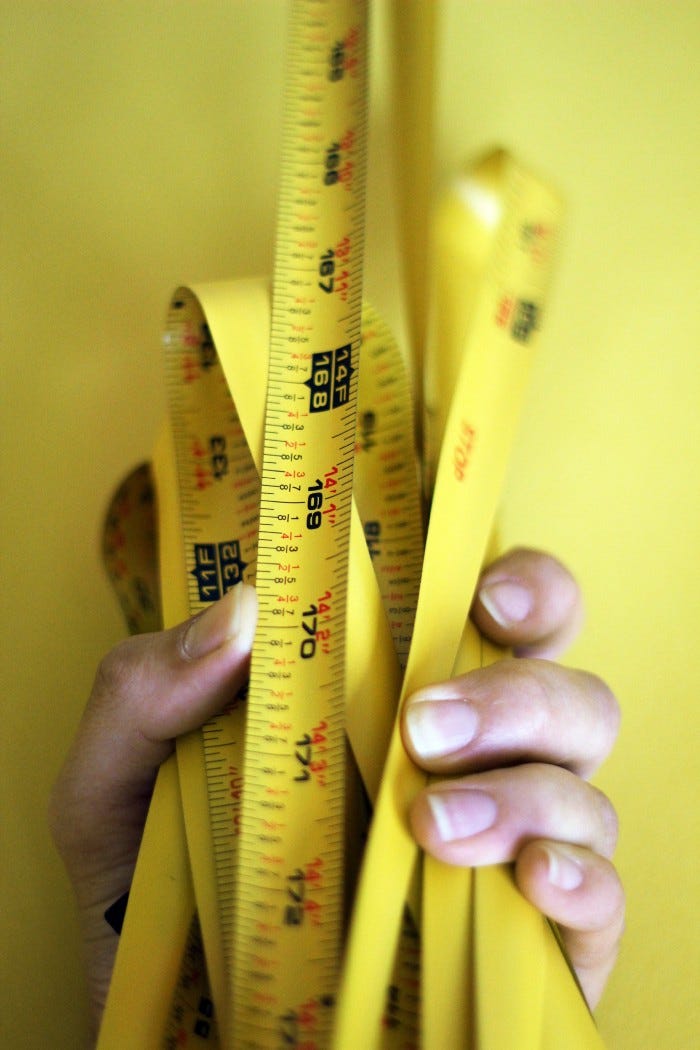 A hand holding a bunched up tape measure together. The 14 Foot marker is visible in the foreground, with several bunches of previous measurements behind it.