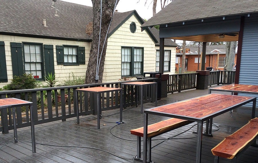 Image description: This is the outdoor patio at a cafe in Houston, Texas with five wooden tables and benches for seating. 