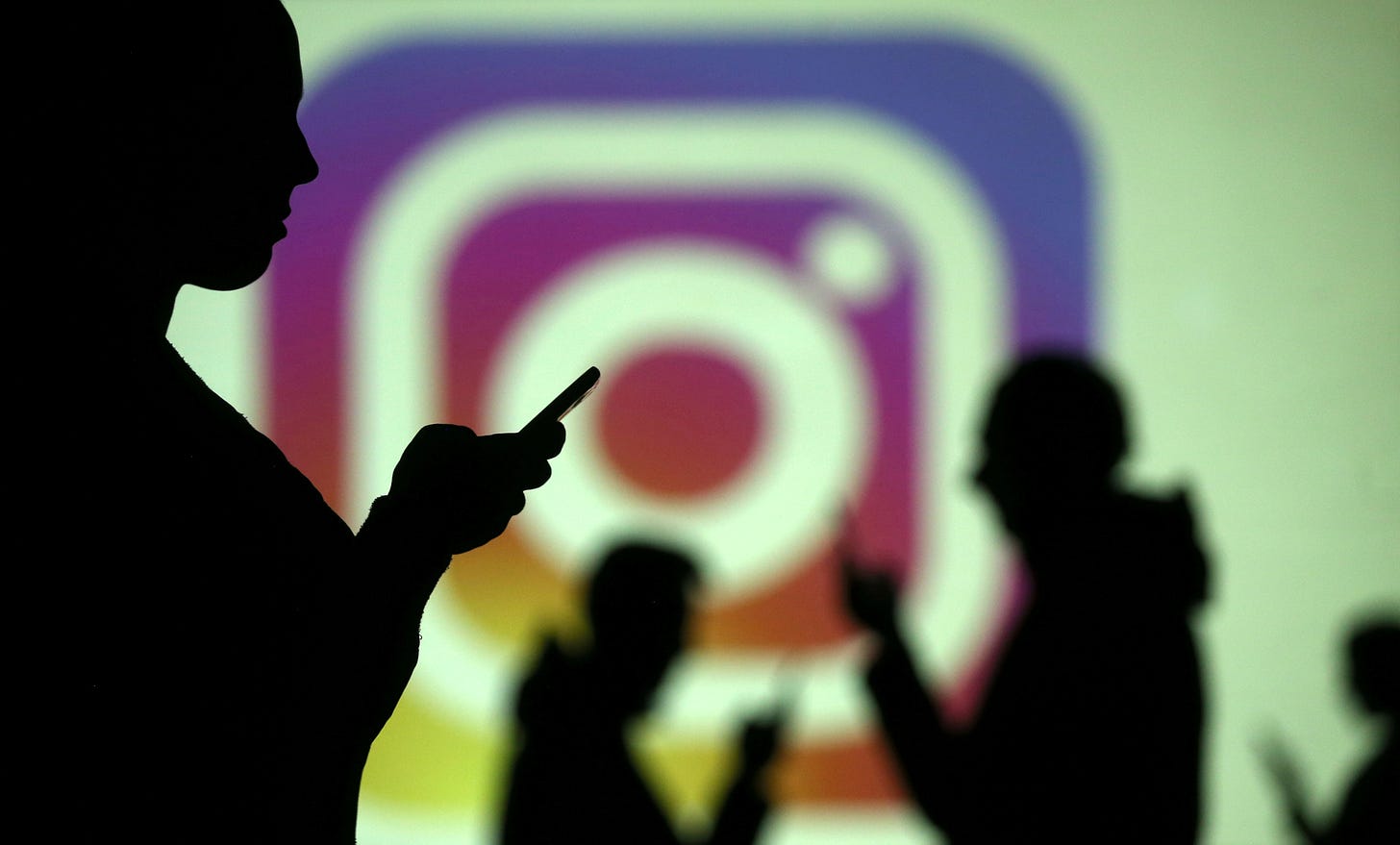 Silhouettes of mobile users are seen next to a screen projection of Instagram logo.  REUTERS/Dado Ruvic