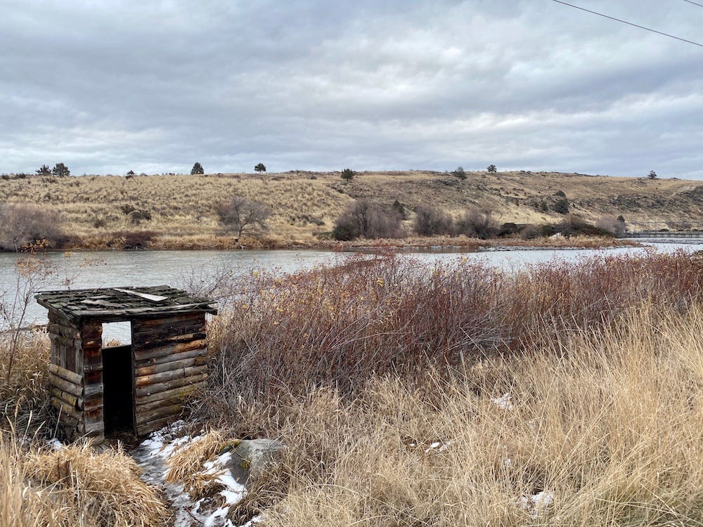 Tiny log fishing hut sits on the bank of the Klamath River, surrounded by tall golden grasses