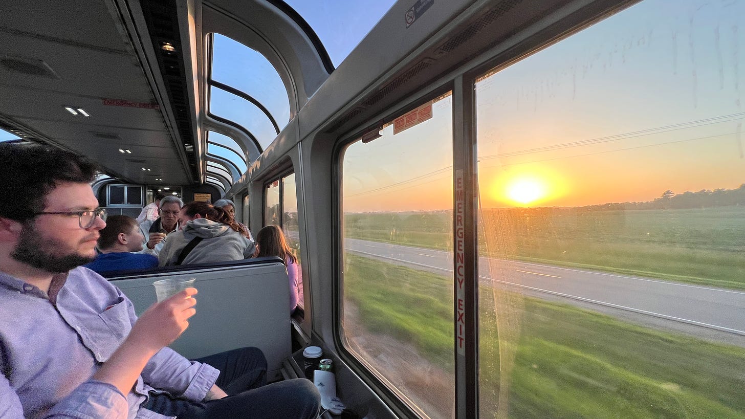 the author, sipping a whisky ginger in a plastic cup, sitting in the observation car watching the sun set over rolling fields