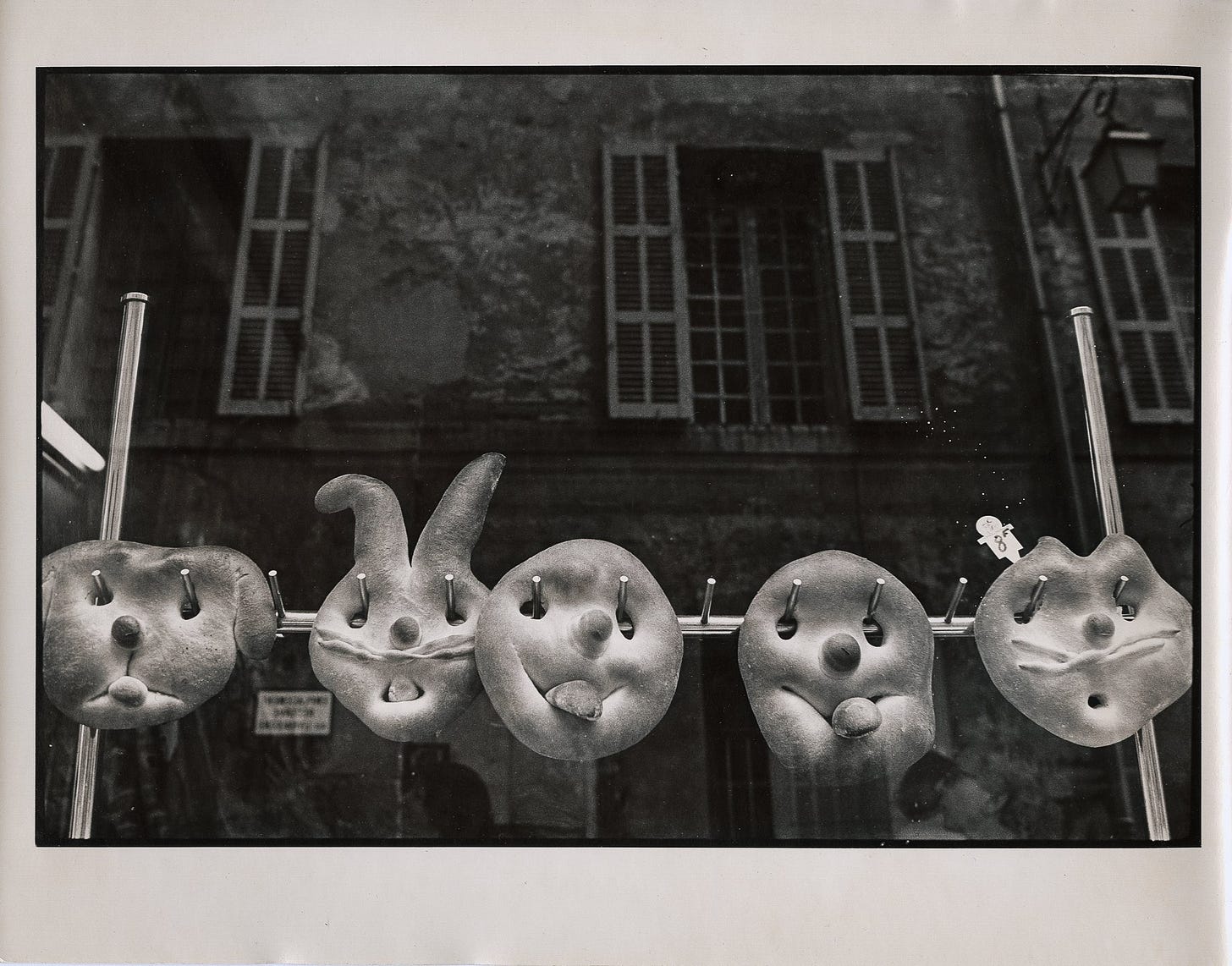 a photograph of French bread, shaped into faces with tongues sticking out, hanging in the window of a bakery