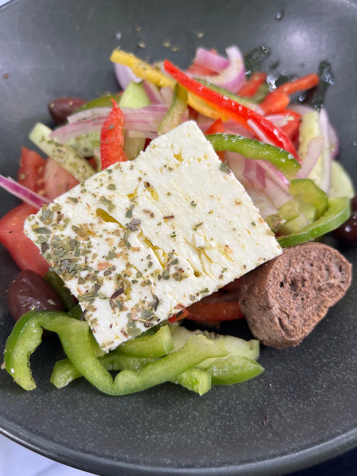 A Greek salad with feta, red onions, green peppers, cucumbers, olives, olive oil and oregano