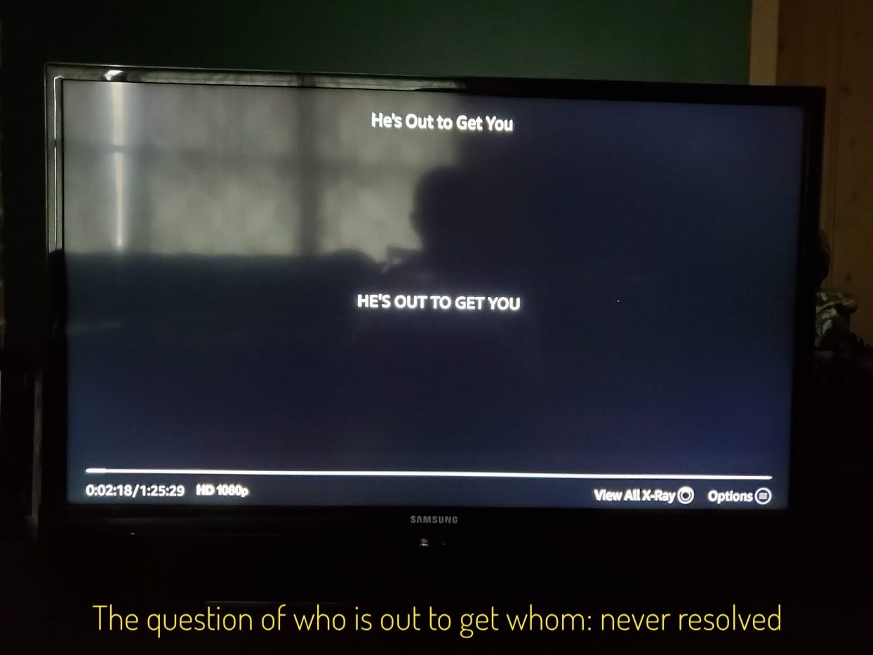 A black screen with “HE’S OUT TO GET YOU” in tiny little letters in the middle of the screen, captioned “The question of who is out to get whom: never resolved”