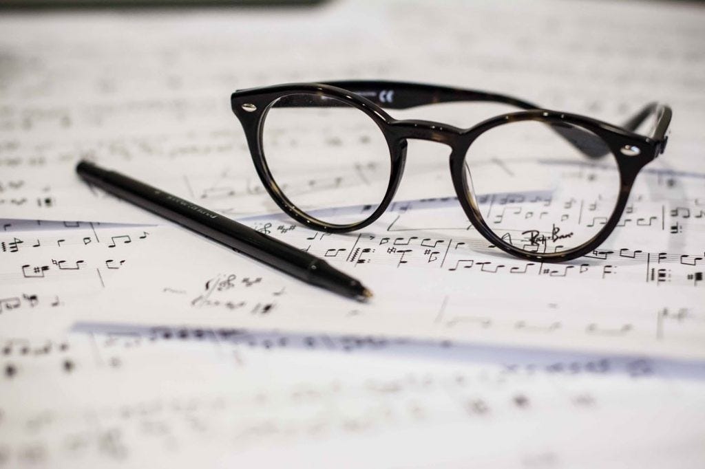 close up of a pair of glasses and a pen on top of a sheet of music