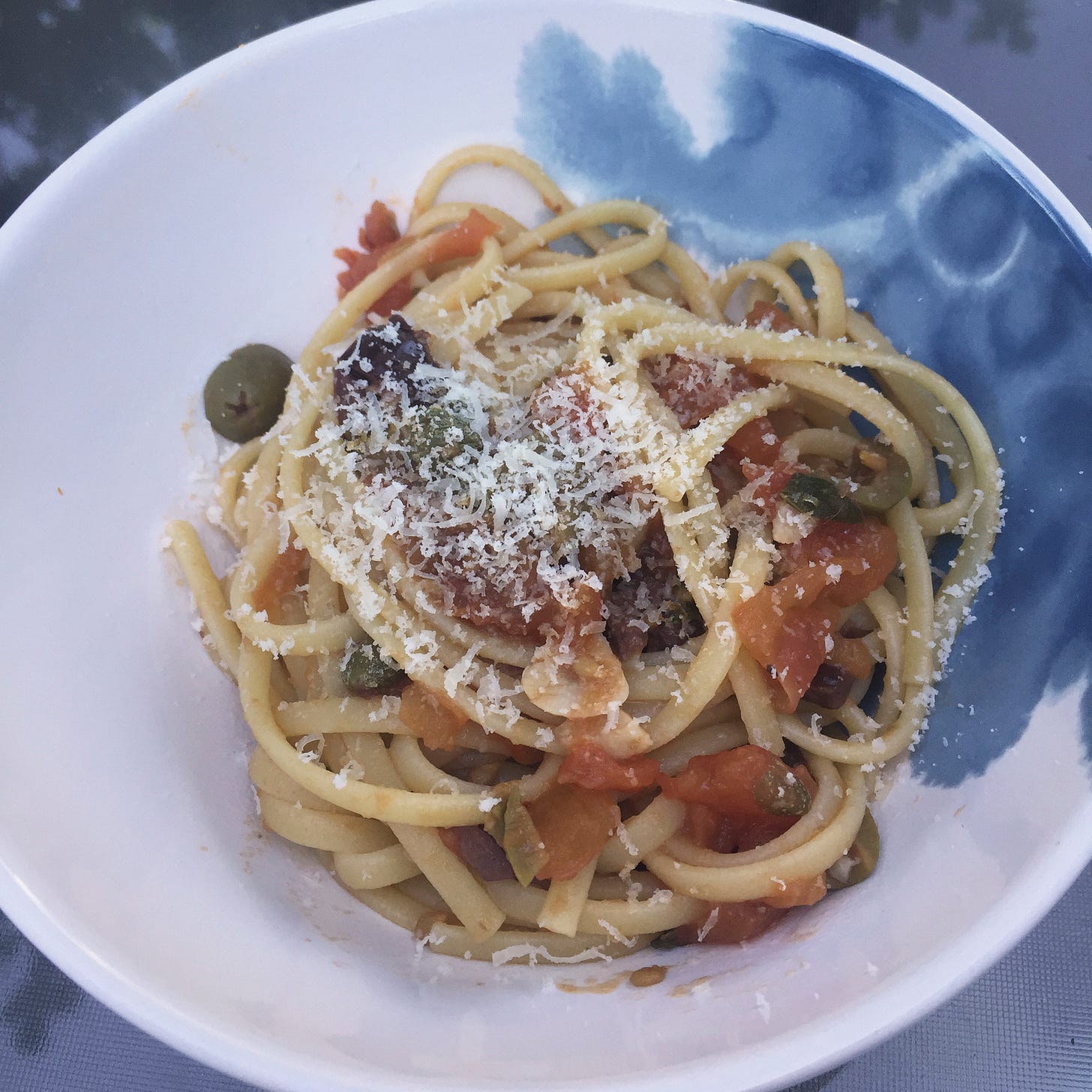 A blue and white bowl with linguine in puttanesca sauce, with parmesan overtop.