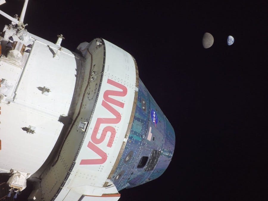 A spacecraft in the foreground and a gibbous moon and Earth in the far distance in space