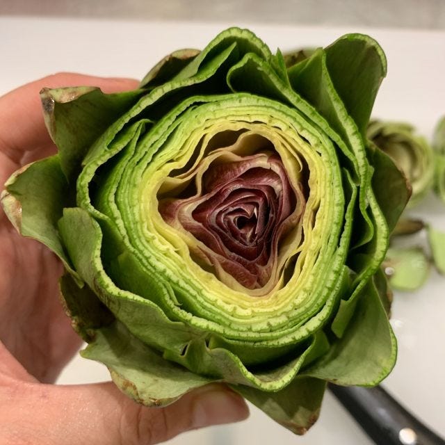 An artichoke with the top cut off, revealing layers of green leaves, fading to purple at the center
