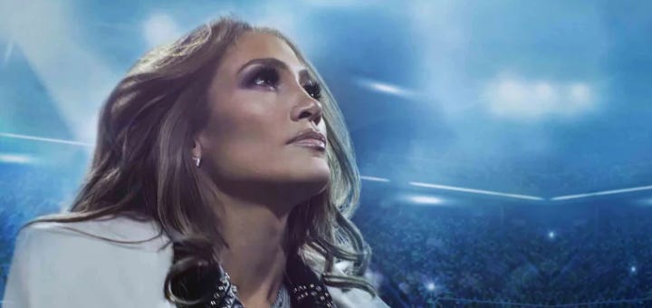 A woman (Jennifer Lopez) looking up, with what appears to be a stadium full of people in the background