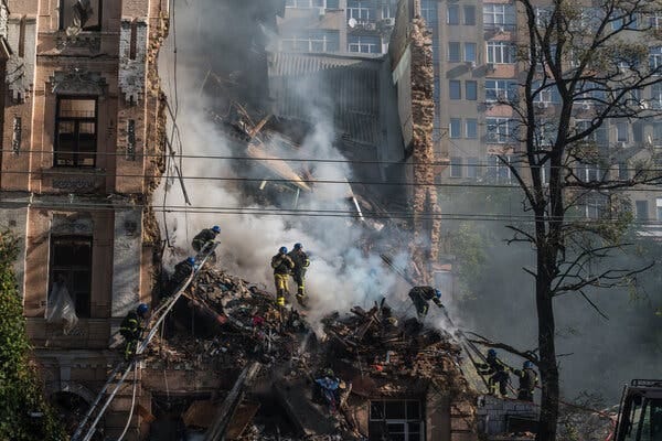 Gray plumes appear beside rescue workers on top of a destroyed building.