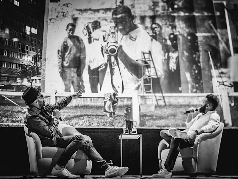 Artist JR (left) and Baratunde (right) sit in front of one of JRs first photographs