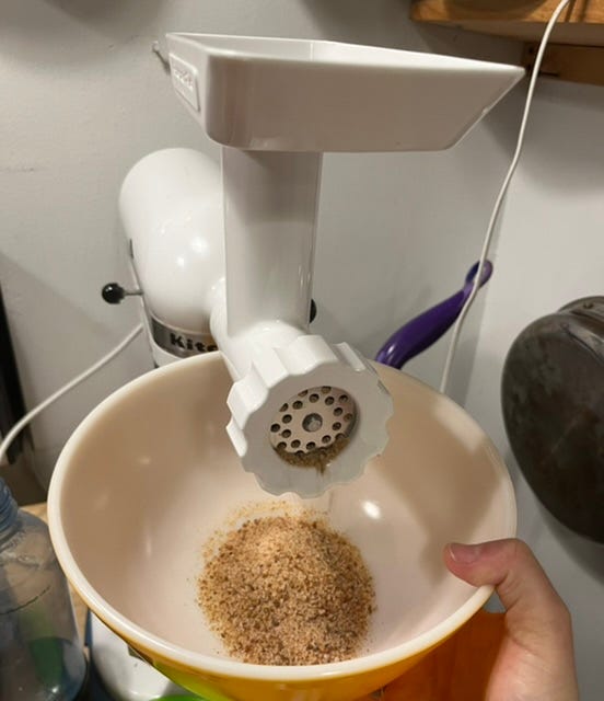 I am holding a bowl of breadcrumbs under a KitchenAid stand mixer with the grinder attachment attached.