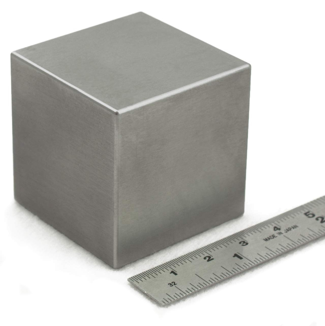 Picture of a 1.5 inch tungsten cube, which looks like a grayish-silver metal cube, with a ruler next to it showing that yup, that’s one point five inches sure enough.