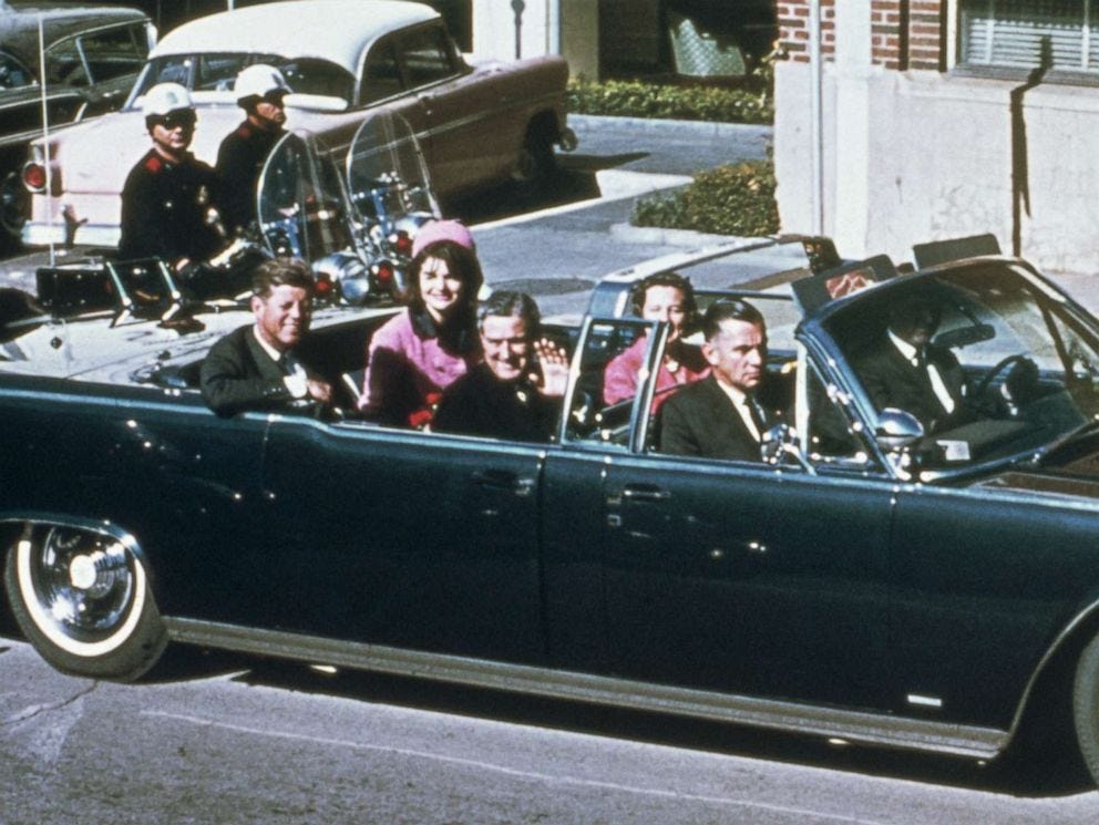 This image shows President John F. Kennedy's 23 November 1963 motorcade. The president sits in the back seat of an open-topped car with with First Lady Jacqueline Kennedy. In front of them, in the vehicle's middle seat, sit Texas Governor John Connally (who waves at the off-camera crowd) and First Lady of Texas Nellie Connally, seated next to her husband. Two Secret Service agents sit in the front seat's driver's and passenger's positions. Two Texas motorcycle police officers ride next to the vehicle's back left side. This image shows President John F. Kennedy's 23 November 1963 motorcade. The president sits in the back seat of an open-topped car with with First Lady Jacqueline Kennedy. In front of them, in the vehicle's middle seat, sit Texas Governor John Connally (who waves at the off-camera crowd) and First Lady of Texas Nellie Connally, seated next to her husband. Two Secret Service agents sit in the front seat's driver's and passenger's positions. Two Texas motorcycle police officers ride next to the vehicle's back left side.