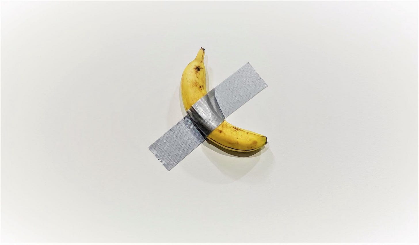 A banana taped to a wall with silver duck tape.