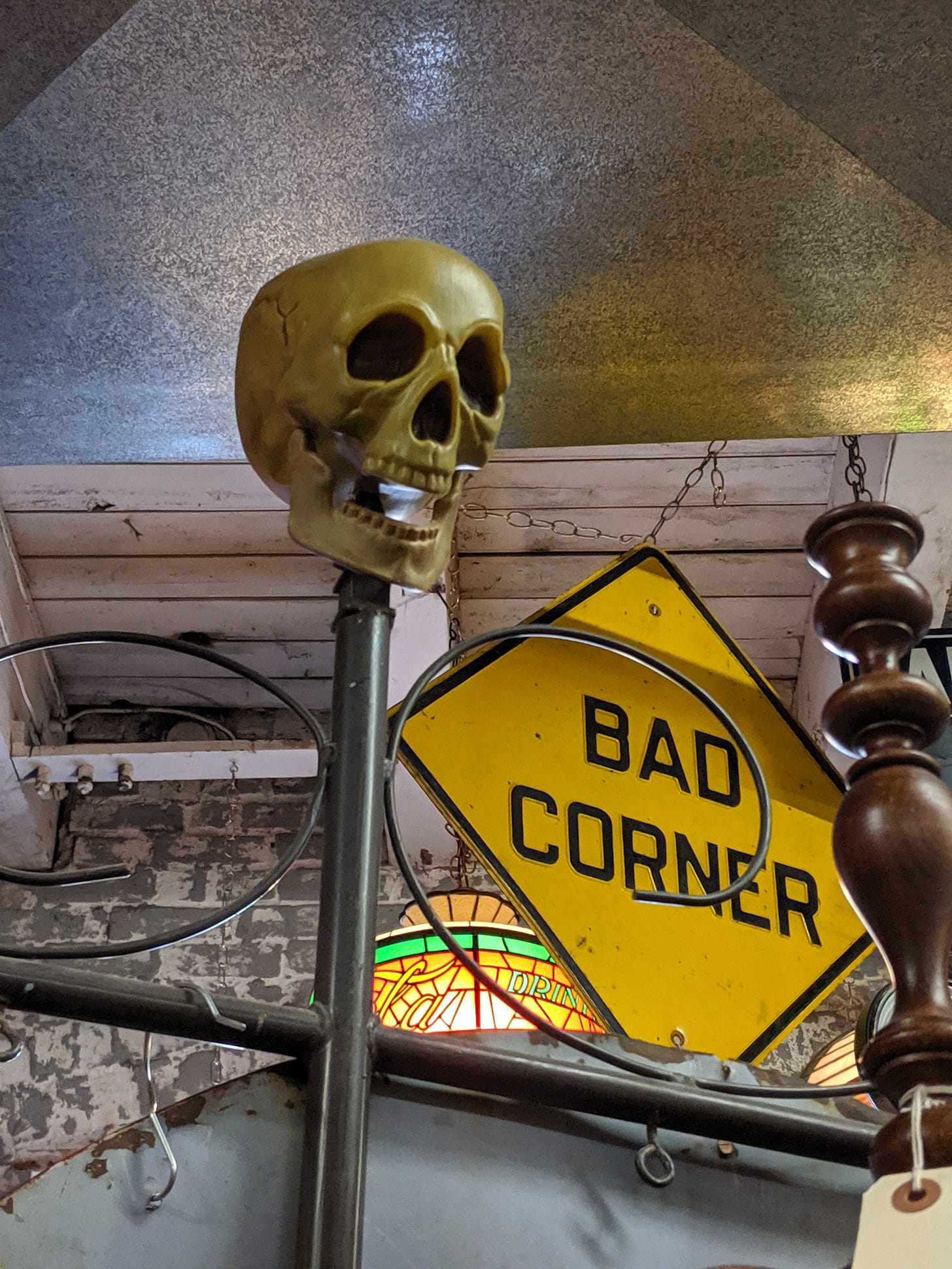 photograph: a plastic skull, a yellow diamond-shaped road sign saying BAD CORNER, and pieces of a brick wall, a bedframe, and maybe a stained glass window
