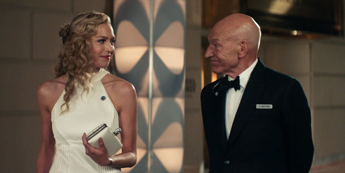 This image shows Jean-Luc Picard (played by Sir Patrick Stewart, on the right) wearing a tuxedo and chatting with Renée Picard (played by Penelope Mitchell, on the left), who wears an elegant, white formal dress. They do so during the Europa Mission gala that Renée is required to attend the night before she and her fellow crew members enter quarantine. This image shows Jean-Luc Picard (played by Sir Patrick Stewart, on the right) wearing a tuxedo and chatting with Renée Picard (played by Penelope Mitchell, on the left), who wears an elegant, white formal dress. They do so during the Europa Mission gala that Renée is required to attend the night before she and her fellow crew members enter quarantine.