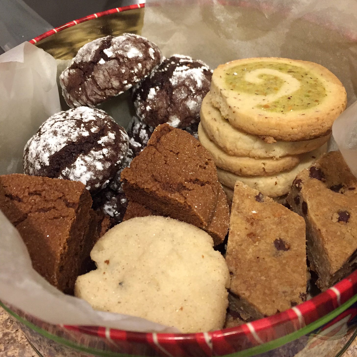 A cookie tin lined with parchment and filled with five types of cookies.