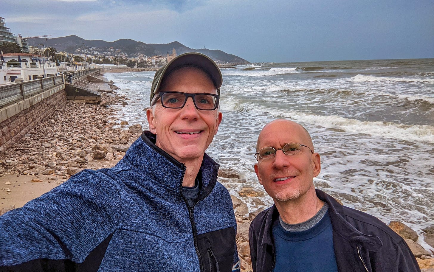 Michael and Brent standing on a rocky beach, the waves rolling in behind them under a grey sky. 